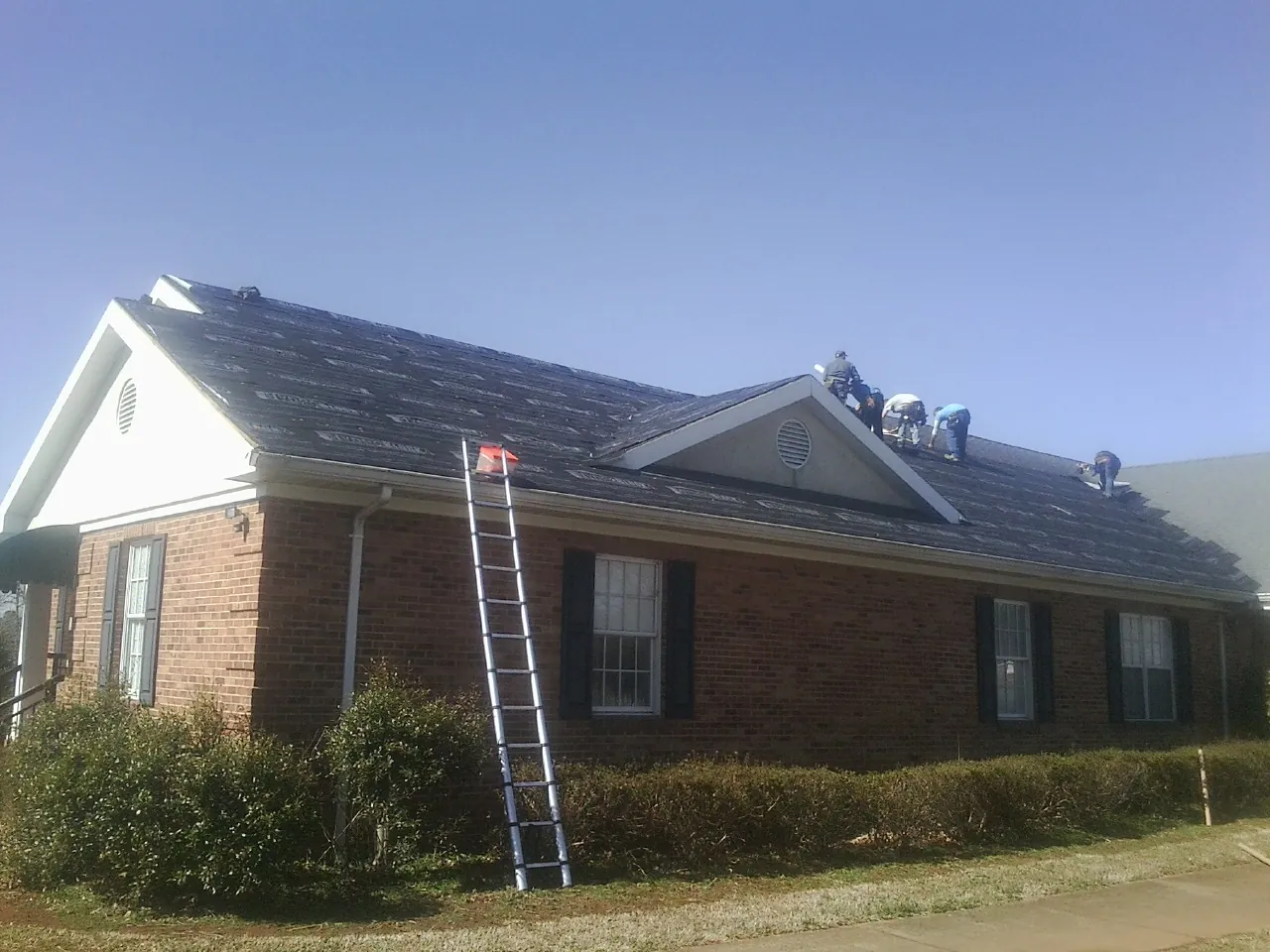 Crew tearing shingles off a brick ranch roof with a ladder set — Emergency Roof Repair work by our crew in Magnolia